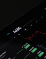 A digital stock trading interface with the focus on AMC Entertainment Holdings, Inc. The screen displays various financial data including stock prices, volume, and market cap. A red line graph shows stock performance over time and several buttons allow for different time frame selections like 1W, 1M, and 1Y. Various stock metrics appear in rows and columns.