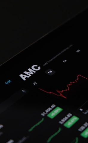 A digital stock trading interface with the focus on AMC Entertainment Holdings, Inc. The screen displays various financial data including stock prices, volume, and market cap. A red line graph shows stock performance over time and several buttons allow for different time frame selections like 1W, 1M, and 1Y. Various stock metrics appear in rows and columns.